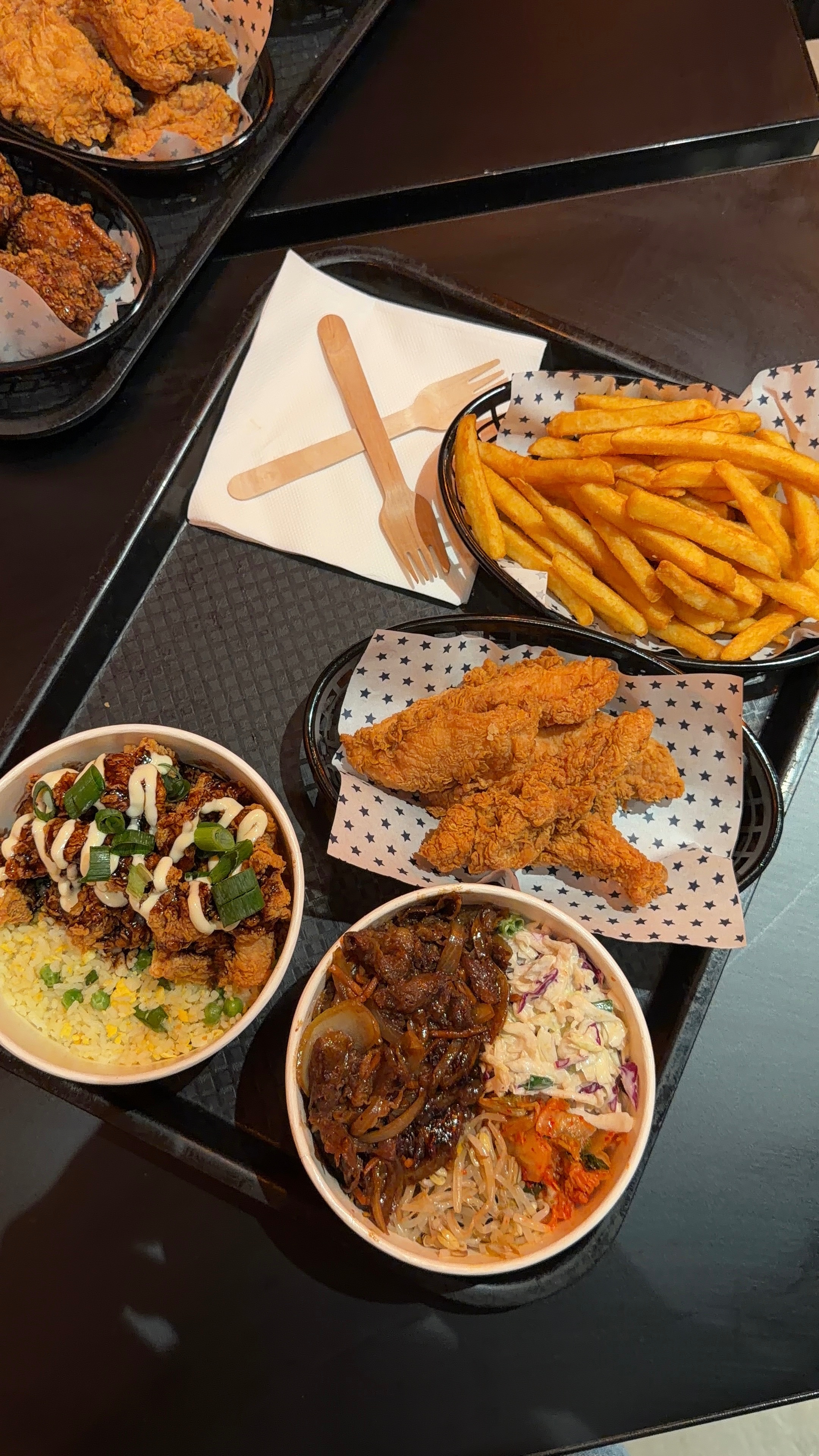A vibrant food spread featuring fried chicken, seasoned fries, and two bowls of rice dishes with various toppings.