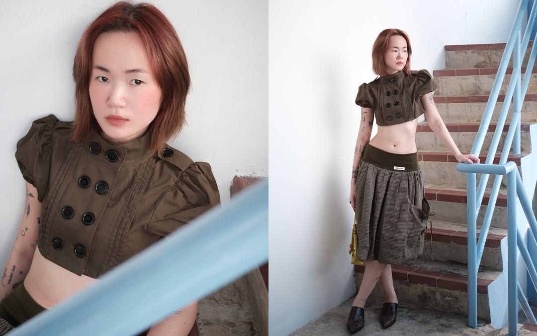 A model poses in a stylish outfit featuring a cropped, button-up top and a long skirt, standing by a blue staircase.