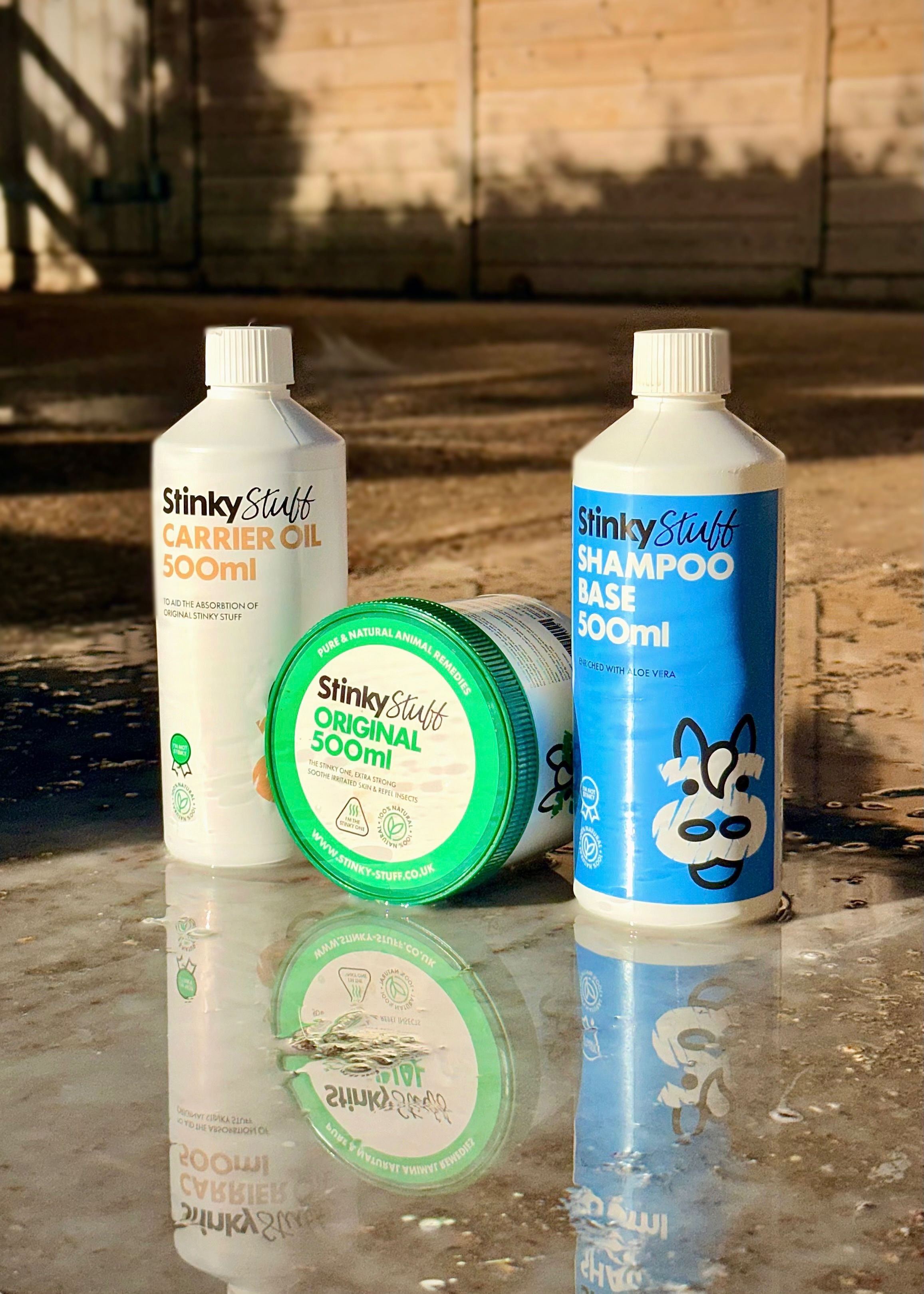 Three bottles of StinkyStuff products, including carrier oil and shampoo base, displayed on a reflective surface.