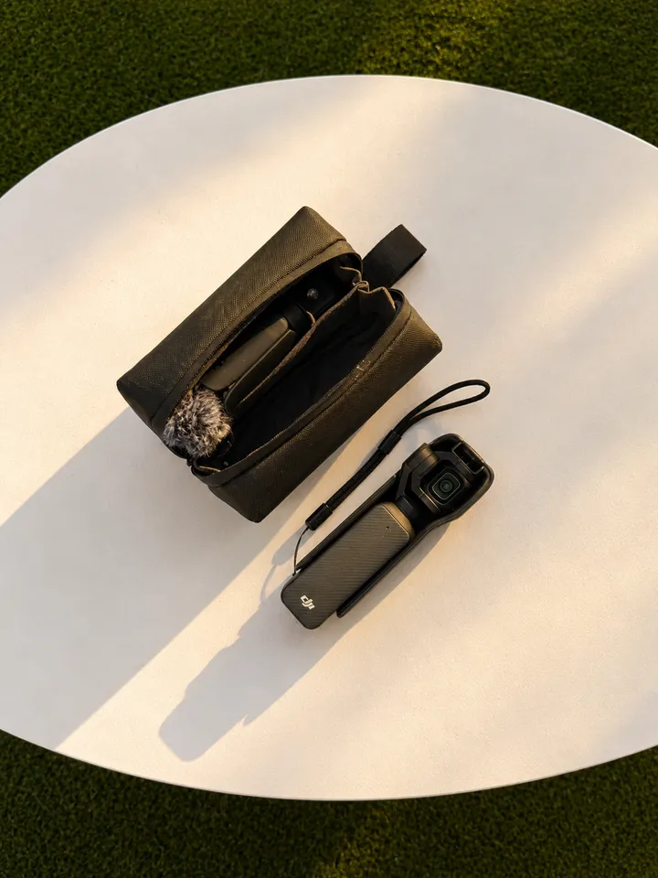 A compact camera placed next to its carrying case on a circular surface, with soft shadows cast by the items.