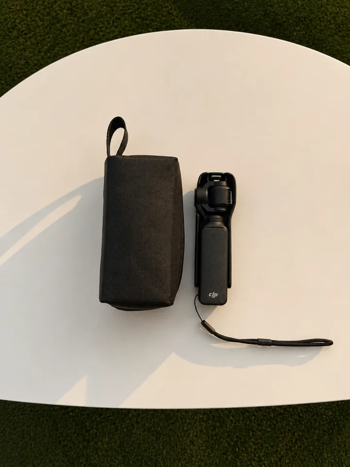 A compact black camera stabilizer placed next to its carrying case on a white table.