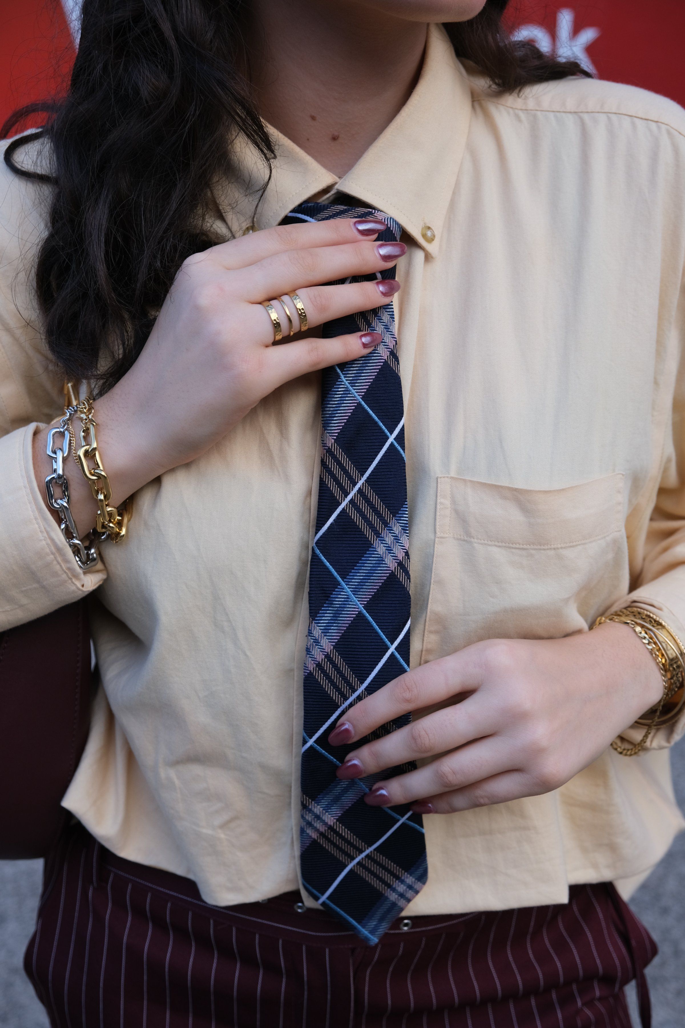 A close-up of a person adjusting a patterned tie while wearing a light-colored shirt and stylish accessories.