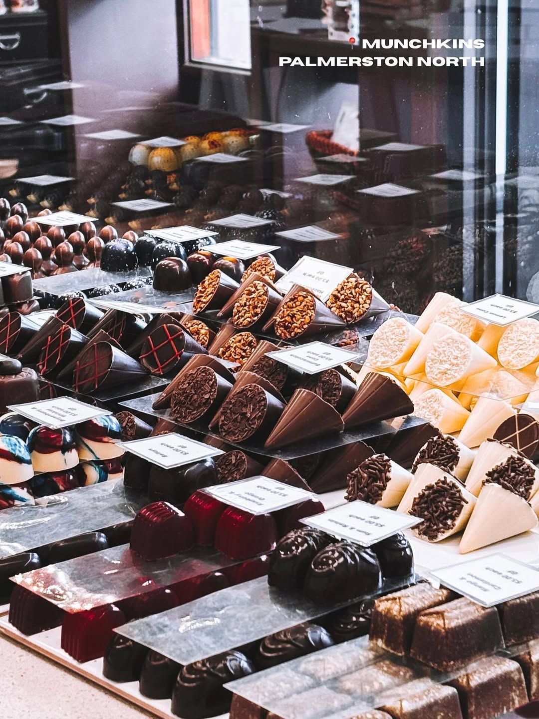 A display of assorted chocolates arranged neatly in a shop, showcasing various shapes and flavors with labels.