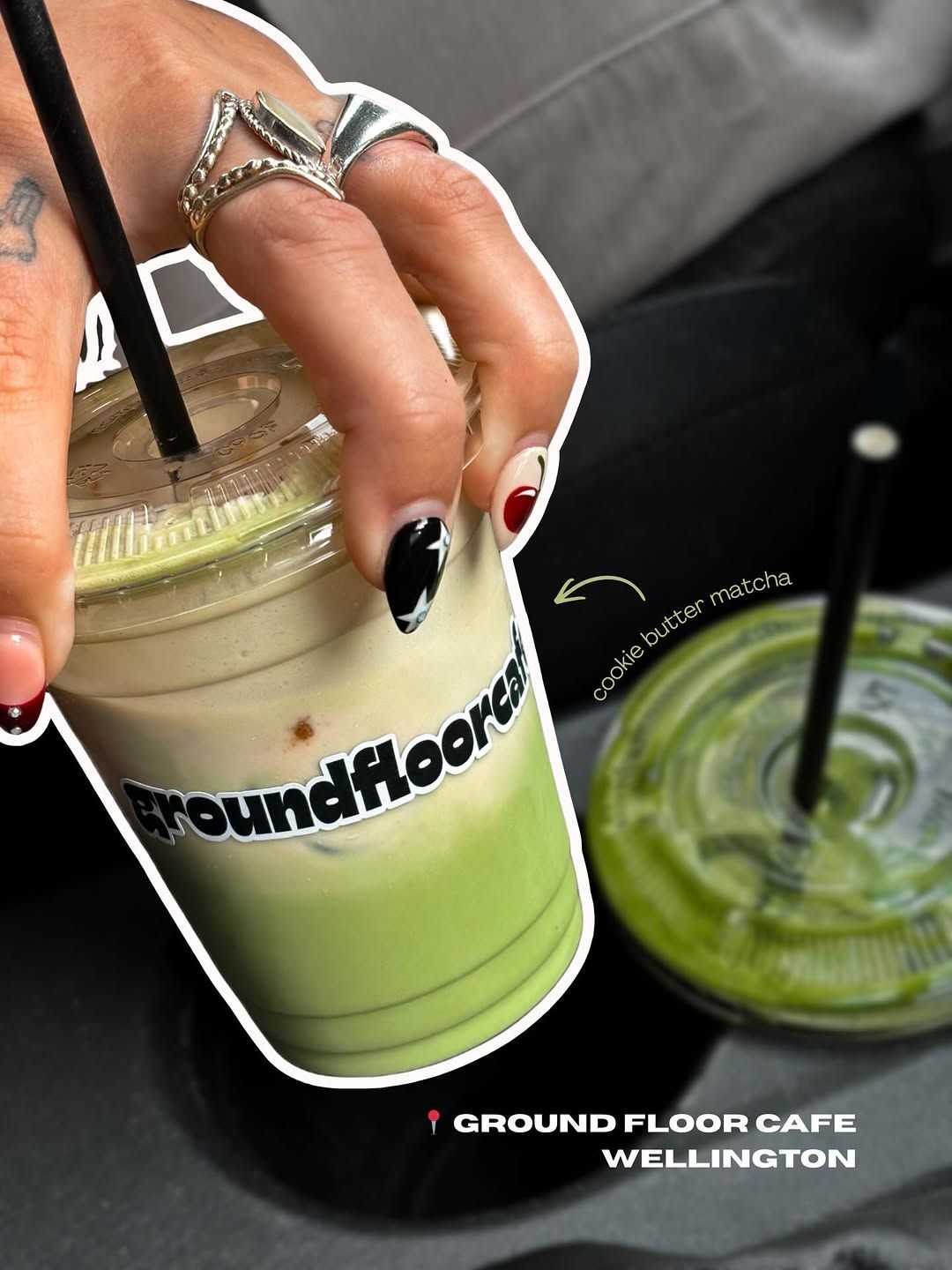 A hand holding a cup of cookie butter matcha from Ground Floor Cafe in Wellington, with another drink visible in the background.