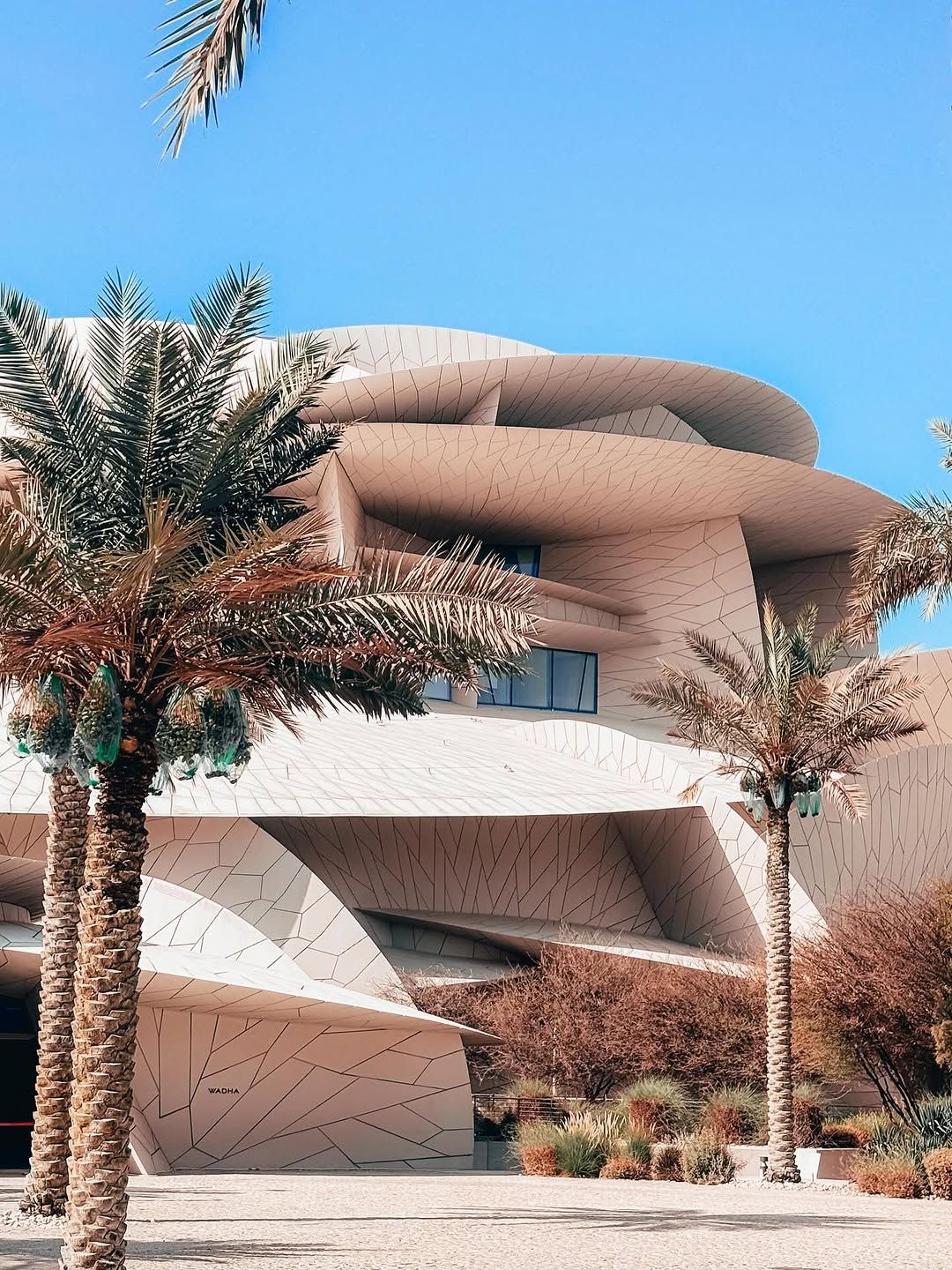 A modern architectural building with a unique design, surrounded by palm trees under a clear blue sky.