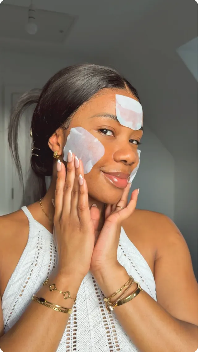 A woman applies skincare patches on her forehead while smiling, showcasing a relaxed beauty routine.