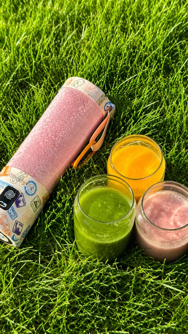 Four colorful smoothie drinks placed on green grass, showcasing vibrant colors and textures.