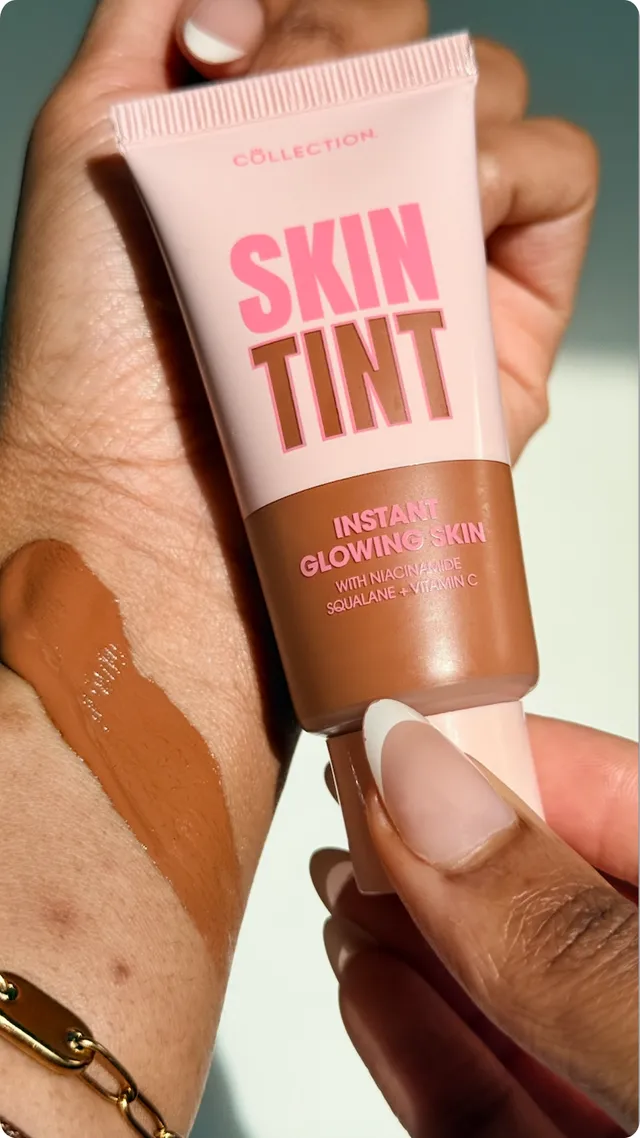 A hand holding a tube of skin tint with a swatch applied on the wrist, showcasing the product's color and texture.