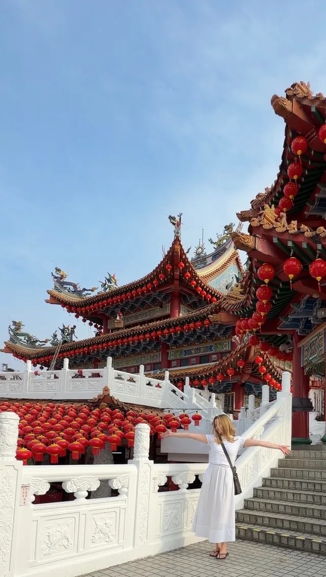 A woman in a white dress stands with her arms outstretched in front of a traditional Chinese temple adorned with red lanterns.